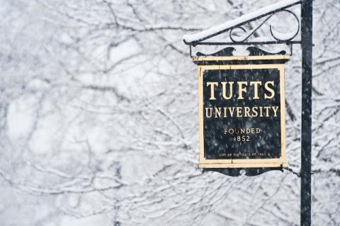 Snow falls on a sign for Tufts University. 