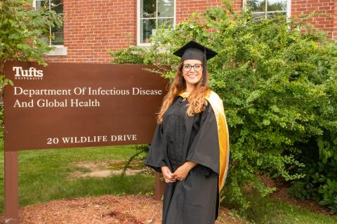 Arielle Potter poses in graduation robes standing in front of the sign for the Department Of Infectious Disease And Global Health
