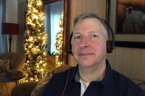 Paul Hogan, wearing headphones, sits in front of a Christmas tree.