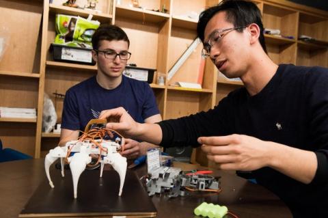 Two students at a makerspace, with a hexapod robot one is building