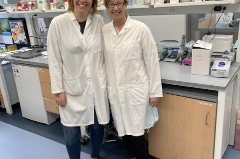 two female researchers in lab coats posing for a picture in their laboratory