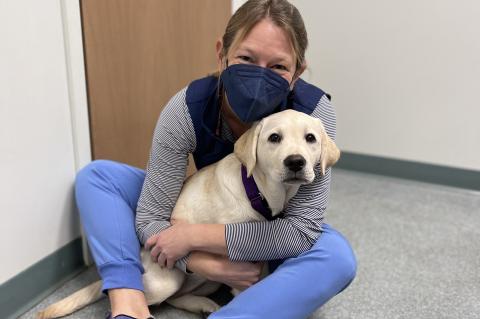 woman wearing a mask sitting on the floor holding her yellow labrador retriever