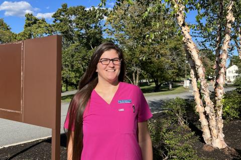 veterinary technician wearing a dark pink medical shirt and standing outside by a tree