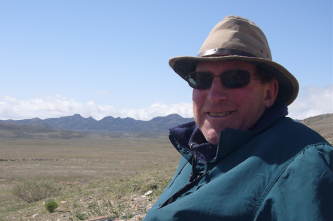 Man in glasses and hat on a plateau with grass and mountains. 