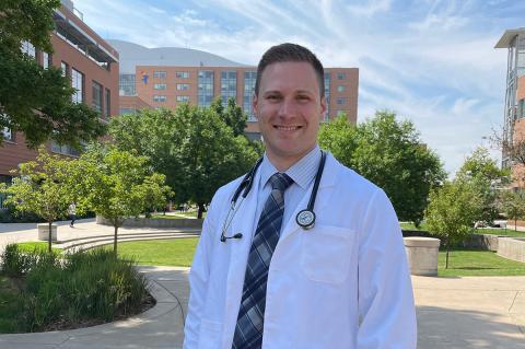 Male graduate student posing for picture in his white coat with stethoscope around his neck