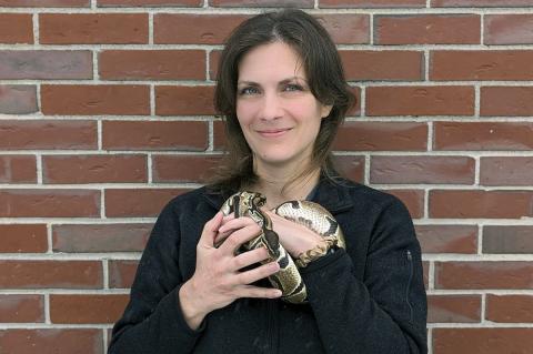 Woman with dark hair holding a ball python while standing in front of a brick wall.