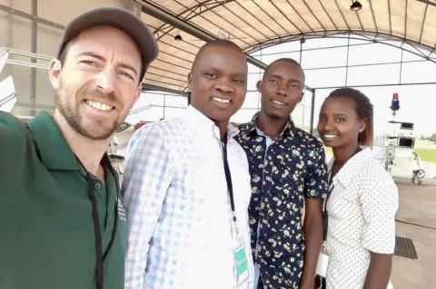 A caucasian man, two Black men, and a Black woman smile as they take a selfie photo in Rwanda.