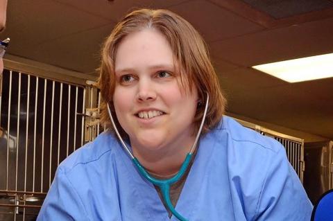 A female veterinarian with red hair wearing blue scrubs and stethoscope around her neck.