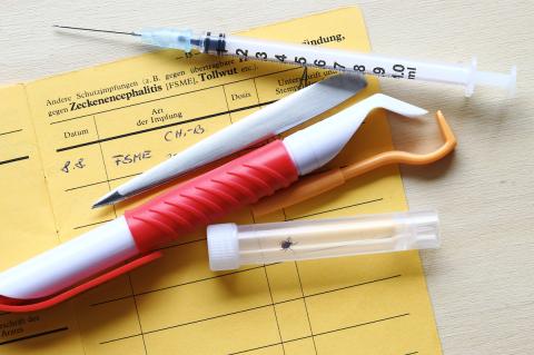 Vaccination against tick-borne encephalitis with vaccination card, syringe and tick tongs stock photo
