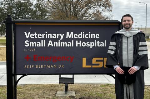 a person dressing in Commencement cap and gown stands next to a campus sign that says 'Veterinary Medicine, Small Animal Hospital, LSU'.