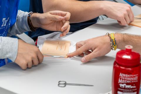  Person using a suture pad up close with silver suture tools.