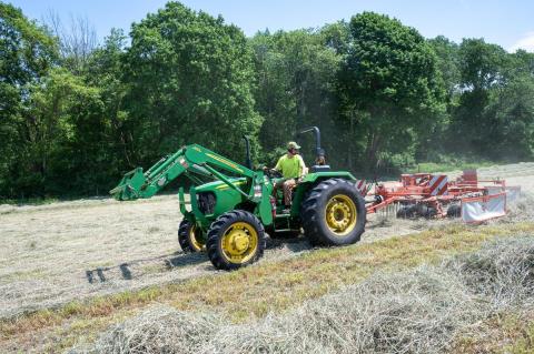 Green tractor in a field gathering grass to make hay.
