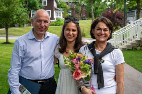 Three smiling people, one holding flowers, standing together. 