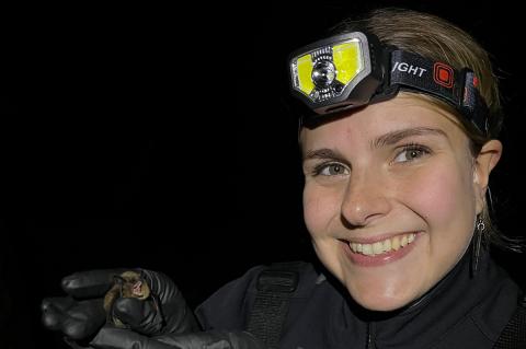 Person smiling in the dark with a headlamp on holding a bat