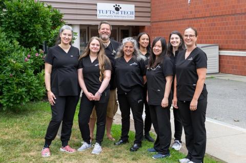 Group of people all wearing black scrubs stand in front of Tufts at Tech Community Clinic building.