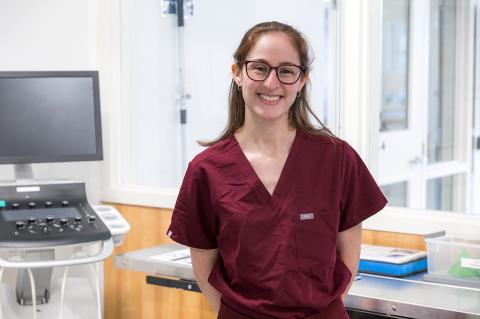 A person smiling with brown glasses while wearing maroon scrubs.