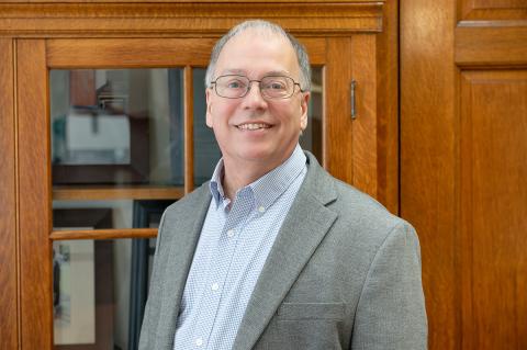Person with glasses and grey blazer smiling.