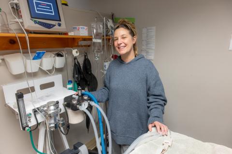 Person wearing grey sweatshirt, smiling, standing next to an anesthesia machine.