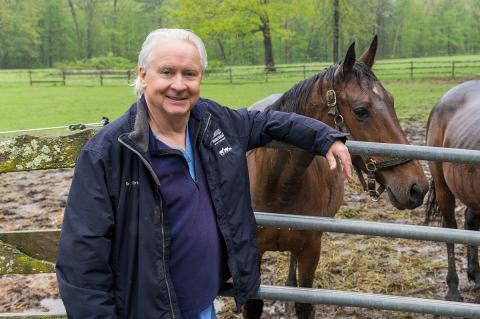 Professor Emeritus Carl Kirker-Head leaning against a railing with horses in the background.