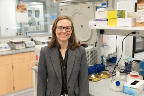 Person with grey blazer and glasses standing in a research lab.