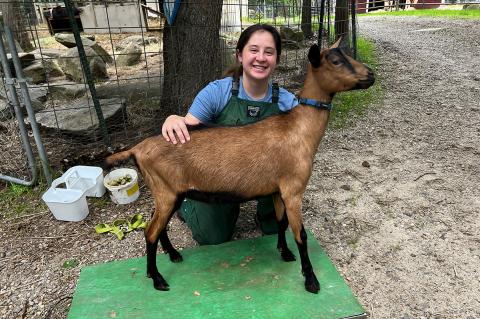 Eleanor Kharasch wearing  green overalls and sitting with a brown goat outside.