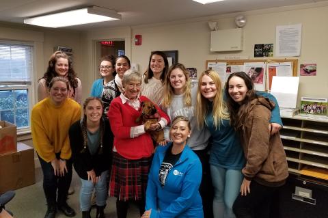 Martha Grace holding her small dog in a classroom with several students smiling around her.